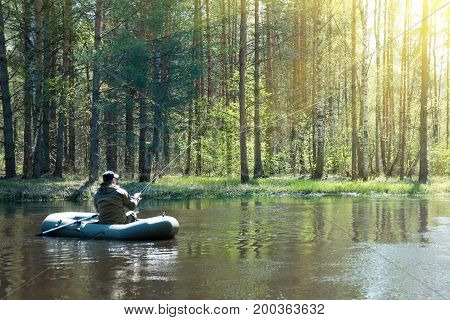 A fisherman in a boat on the river casts a fishing pole