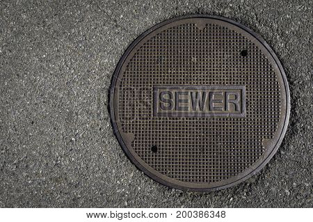 Sewer manhole surrounded by asphalt placed on the right