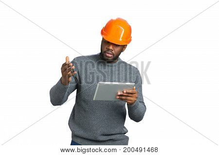 Young male engineer gesticulating with tablet. Dark skinned constructor with tablet raised hand with amazement on white background.
