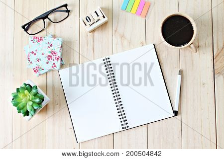 Still life, business office supplies or new year concept : Top view of working desk with blank notebook with pen, coffee cup, colorful note pad, cube calendar and eyeglasses on wooden background