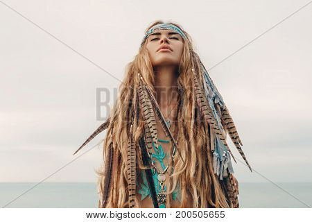 fashion model portrait outdoors. boho style young woman with headdress made of feathers