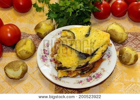 Hot Ready Moussaka Is Served On A Porcelain Plate Among Vegetables And Spicy Herbs. Fresh Vegetables