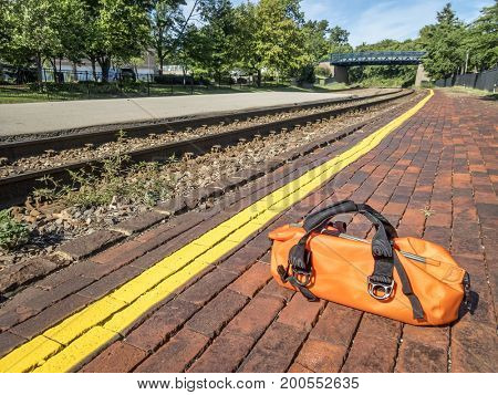 Waiting for a train concept - a bright orange duffel on a station platform behind yellow line