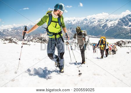 A group of mountaineers rises to the top of a snow-capped caucasian mountain against the backdrop of the rocky peaks of the mountains covered with snow.