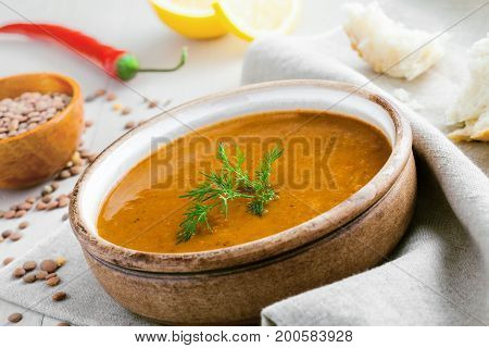 Healthy vegetarian lentil soup in a rustic clay bowl on a white wooden table. Delicious healthy meal served on a canvas tablecloth. Close-up shot.