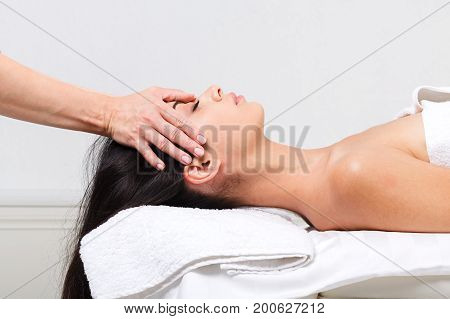Head and face massage in spa. Female beautician work in wellness center. Professional massagist make relax healthy procedure to beautiful indian girl in cosmetology cabinet or beauty parlor.