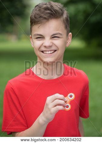 Young teen boy holding popular fidget spinner toy - outdoors portrait. Happy smiling child playing with a orange Spinner in summer park.