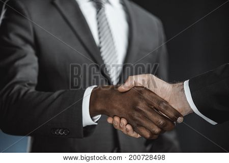 selective focus of multicultural businessmen handshake isolated on black