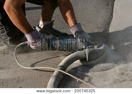 A construction worker is grinding down the concrete edge on a road and curb project and leaving a trail of dust.
