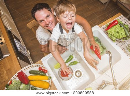 Father with little son washes vegetables on the kitchen before eating