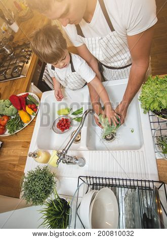 Father with little son washes vegetables on the kitchen before eating