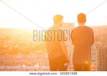 Two men are drinking wine on the roof at sunset. Best friends.