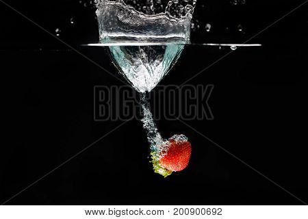 A strawberry splashing into water black background.