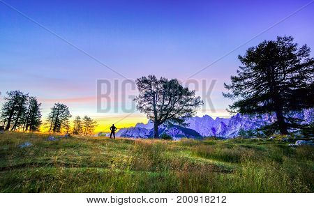 Silhouettes of a man and illuminated tent under a night sky at twilight hour. Recreation hiking and camping. Alps, Triglav National Park, Slovenia.