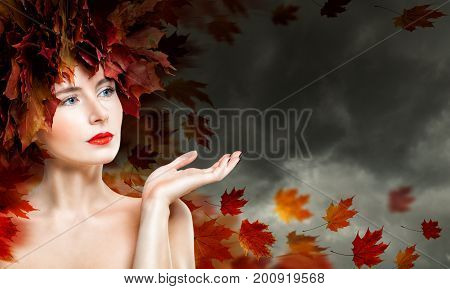 Autumn Woman Showing Empty Copy Space on the Open Hand against Cloudy Sky. Beautiful Fashion Model with Fall Leaves Fantasy Autumn Season Concept