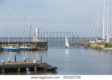 Small Sailboat Sailing Out Of The Harbor Of Hindeloopen In The Province Of Friesland, The Netherland