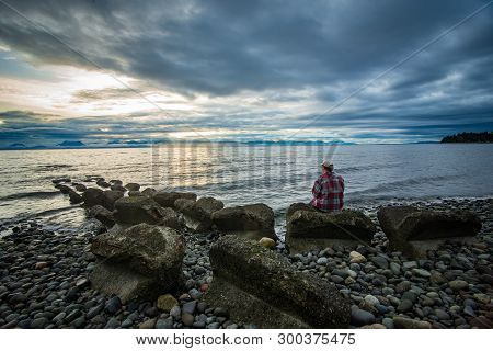 Man Sitting On Miracle Beach In The Comox Valley, British Columbia, Canada