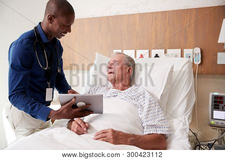 Doctor With Digital Tablet Visiting And Talking With Senior Male Patient In Hospital Bed