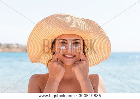 Smiling Woman In Hat Is Applying Sunscreen On Her Face. Indian Style