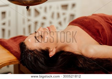Relaxed Young Woman Lying Under Shirodhara Vessel During Ayurvedic Procedure