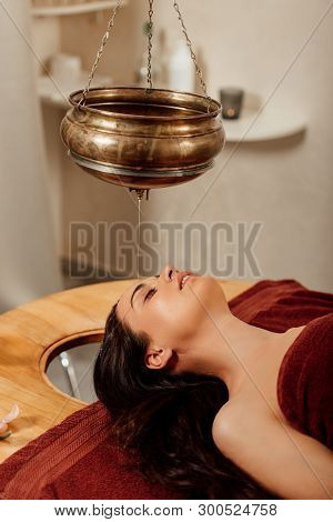 Relaxed Young Woman Lying Under Shirodhara Vessel During Ayurvedic Procedure
