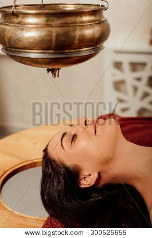 Relaxed Young Woman Lying Under Shirodhara Vessel During Ayurvedic Procedure