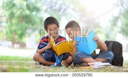 Two Boys Of Primary Reading And Doing Homework Together.