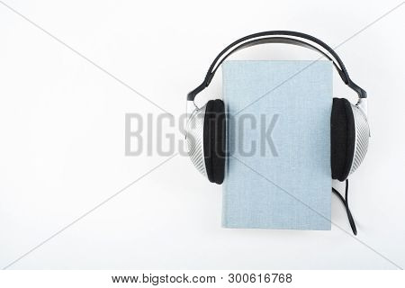 Audiobook On White Background. Headphones Put Over Blue Hardback Book, Empty Cover, Copy Space For A