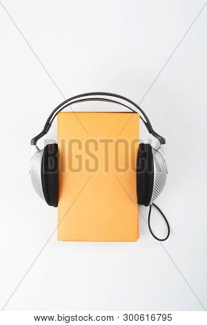 Audiobook On White Background. Headphones Put Over Yellow Hardback Book, Empty Cover, Copy Space For