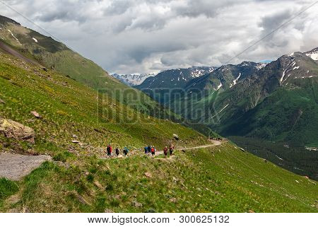 Group Of People Men And Women Walk On Mountain Range Covered With Green Grass. Tourists Go On Mounta