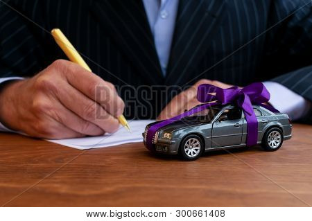 Man Is Signing A Vehicle Sales Contract. Automobile As A Gift