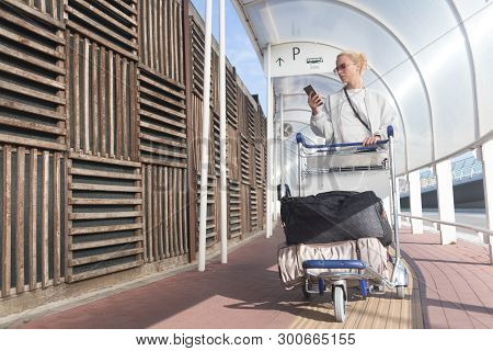 Young Casual Woman Using Mobile Phone Application While Transporting Luggage From Arrival Parking To