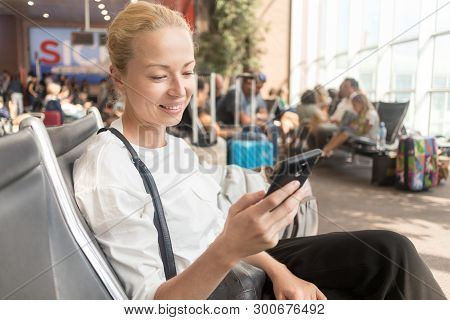 Female Traveler Reading On Her Cell Phone While Waiting To Board A Plane At Departure Gates At Airpo