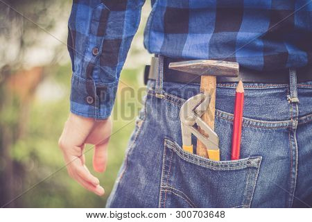Home Handyman: Rear View Of A Young Man With Hammer, Pencil And Gripper In His Pocket