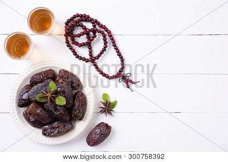Ramadan Food And Drinks Concept. Wood Rosary, Tea And Dates Fruit On A White Wooden Table Background