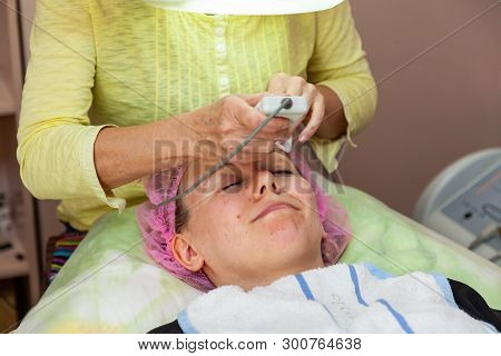 A Young Girl Is Lying On Couch With A Pink Hat On Her Hair While Performing An Ultrasonic Face Clean