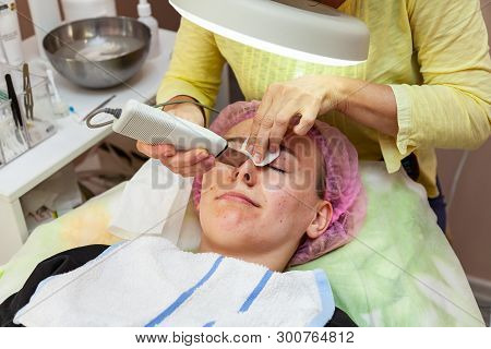 A Young Girl Is Lying On Couch With A Pink Hat On Her Hair While Performing An Ultrasonic Face Clean
