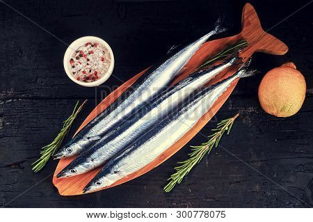 Raw Saury On A Wooden Board In The Form Of Fish With Rosemary And Lemon-top View