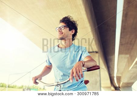 people, style, leisure and lifestyle - young hipster man riding fixed gear bike on city street