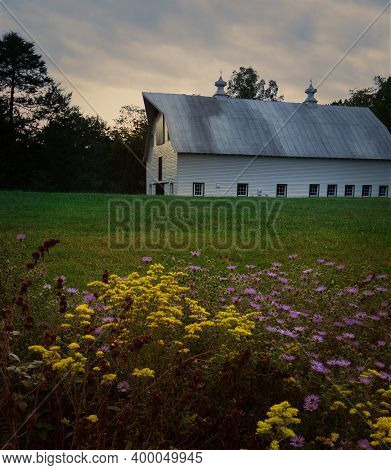 A Rural Barn Is Bathed In Afternoon Glowing Sunlight With Pastel Clouds In The Sky And Colorful Flow