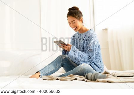 Beautiful Young Asian Woman Wearing Knitted Sweater Sitting In Comfort Using Tablet At Cozy Home Atm