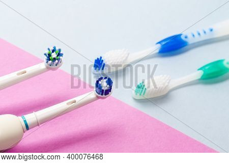 Brushing Heads Of Two Professional Electric Toothbrushes Against Manual Brushes On Pink And Blue Bac
