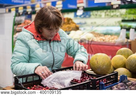 A Woman In A Self-service Supermarket Selects The Most Ripe, Fresh And Delicious Fruits And Vegetabl