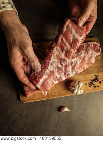 Fresh Pork Ribs, Cooking For Frying With Garlic, On A Wooden Background Top View. Male Hands Holding