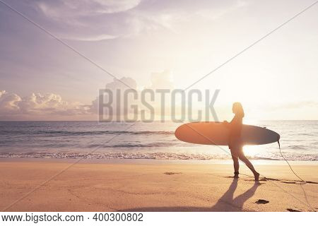 Woman Hold Surfboard Standing At Tropical Sunset Beach Background. Summer Vacation And Sport Adventr