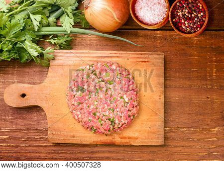 Raw Minced Meat With Herbs And Spices In A Buger Shape On A Wooden Board On A Rustic Wooden Backgrou
