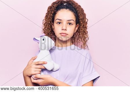Beautiful kid girl with curly hair holding animal doll toy thinking attitude and sober expression looking self confident 