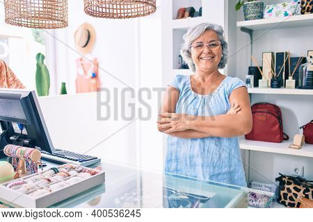 Middle age shop assistance woman working at the counter of retail shop smiling happy