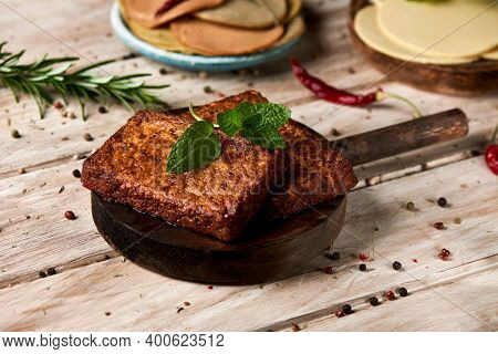 closeup of some tofu fillets on a white rustic table, and some slices of vegan cheese and some cold cuts made of tofu in the background