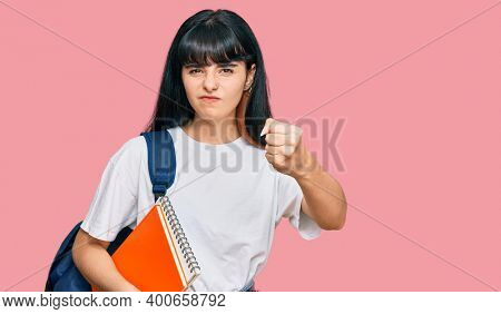 Young hispanic girl wearing student backpack and holding book annoyed and frustrated shouting with anger, yelling crazy with anger and hand raised 